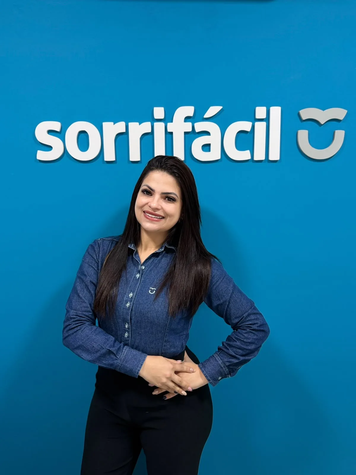 Integrante del equipo de Sorrifácil Jaguarão sonriendo frente al logo de la clínica